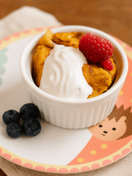 A ramekin of pumpking maple bread pudding is shown with whipped cream and berries on top.