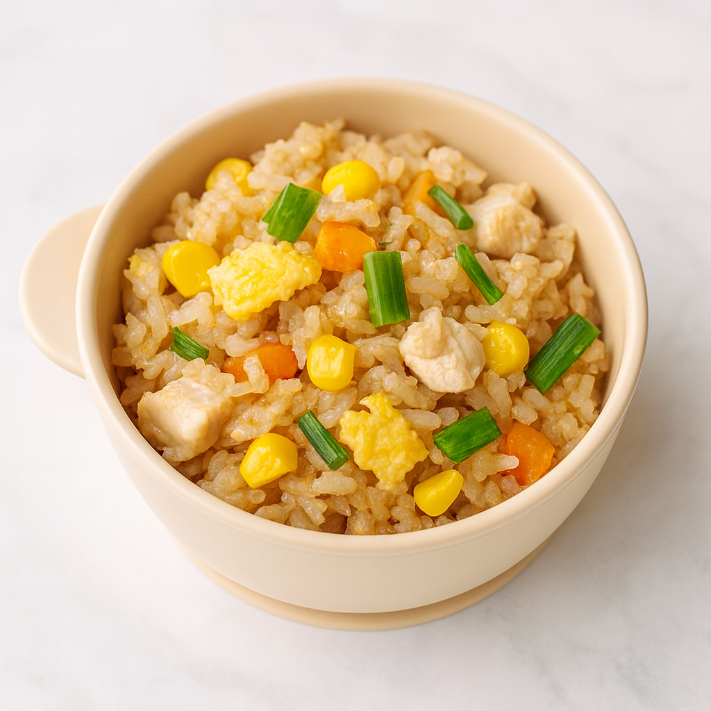 A small bowl is filled with vegetable fried rice for toddlers, with bits of egg, corn, carrot, and green onion visible at top.