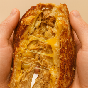 a tuna sandwich for kids is pulled apart to reveal its layers of toasted bread, gooey cheese, potato chips, and tuna.