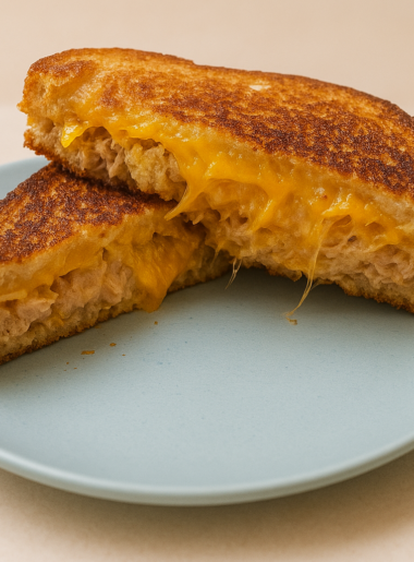 A tuna sandwich for kids is halved and stacked to show its interior of gooey cheese, potato chips, and tuna salad spread.