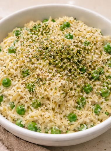 A bowl full of creamy orzo, studded with peas and cheese; herbs are strewn on top.