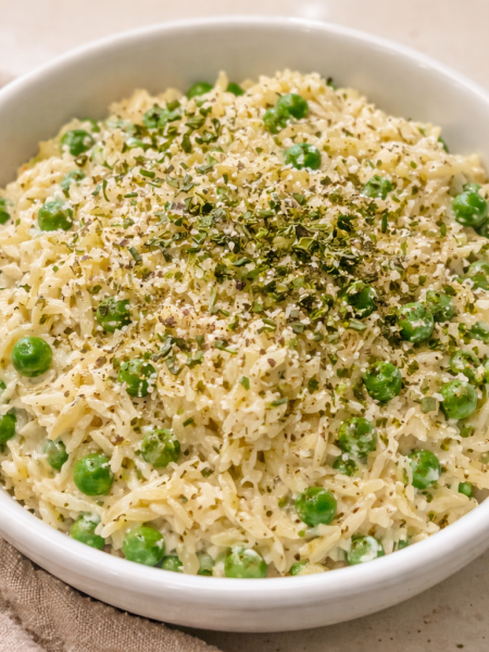 A bowl full of creamy orzo, studded with peas and cheese; herbs are strewn on top.