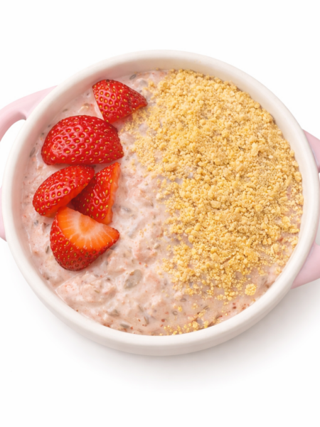 An overhead shot of a toddler's bowl of overnight oats, with a pink-hued bed fo creamy oats topped with cut strawberries and a dusting of graham cracker crumbs.