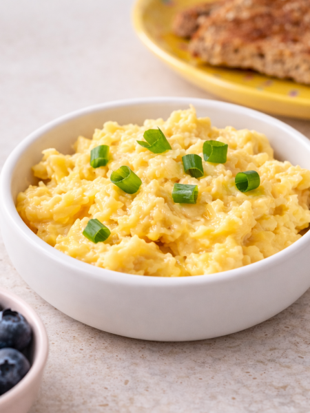 A bowl of soft shirred scrambled eggs for toddlers is sided by toast and fruit.