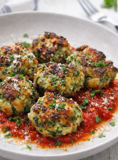 Small spinach and cheese dumplings--known as malfatti--are shown atop tomato sauce, with grated cheese and basil strewn about.