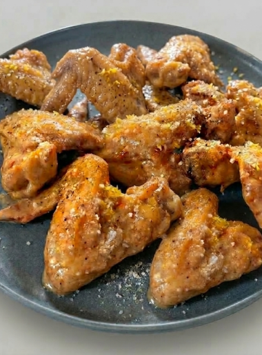 A plate full of 'wet' lemon pepper wings for kids; wings are dusted with lemon zest, parmesan, and black pepper.