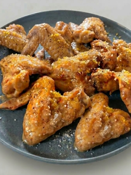 A plate full of 'wet' lemon pepper wings for kids; wings are dusted with lemon zest, parmesan, and black pepper.