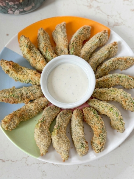 Wedges of crispy air fryer avocado fries surround a ramekin of ranch dressing.