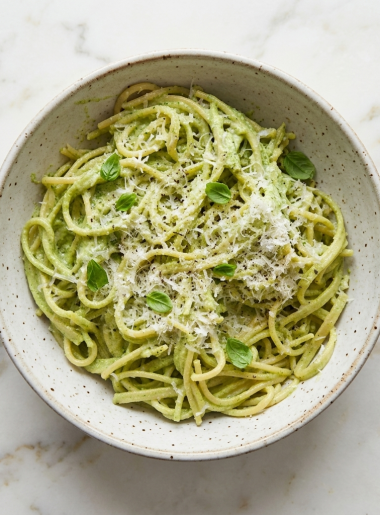 A bowl of high protein green pasta for toddlers, with spaghetti coated in creamy broccoli pesto, is shown on top of a counter.