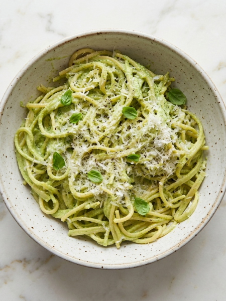 A bowl of high protein green pasta for toddlers, with spaghetti coated in creamy broccoli pesto, is shown on top of a counter.