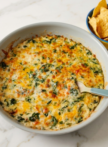 A large pan full of a spinach and cheese dip for kids is sided by a small bowl of tortilla chips with which to dip into the mix.