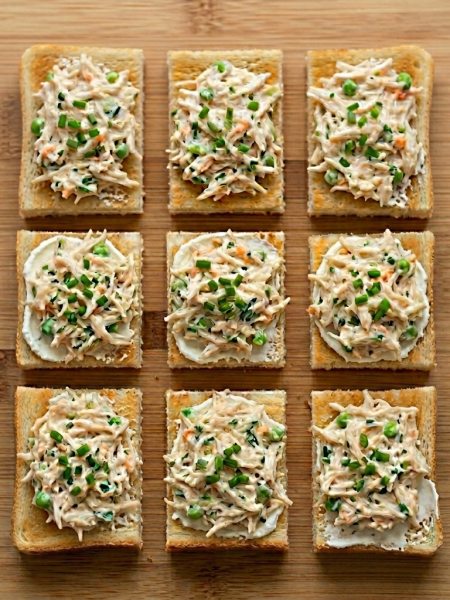 Toast fingers spread with toddler chicken salad and goat cheese are shown lined up on a cutting board.