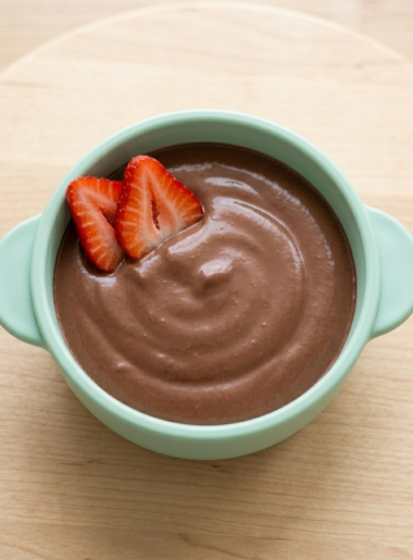 A blue bowl is filled with a high-protein chocolate pudding; two strawberry slices crown the top of the bowl.