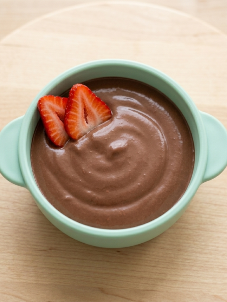 A blue bowl is filled with a high-protein chocolate pudding; two strawberry slices crown the top of the bowl.