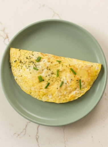 An omelette for toddlers, topped with small slivers of scallion, drapes a gray plate.