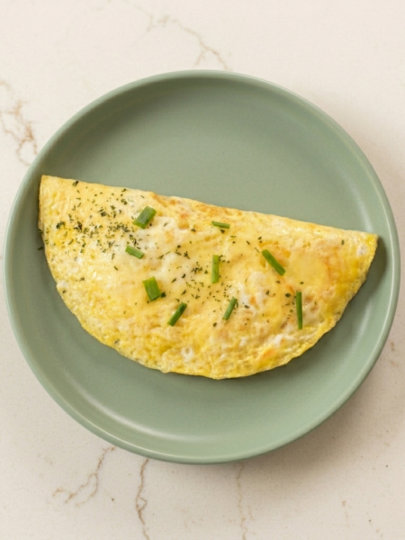 An omelette for toddlers, topped with small slivers of scallion, drapes a gray plate.