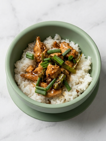 A bowl of toddler three cups chicken, with nubbins of chicken and sticks of asparagus strewn atop white rice.