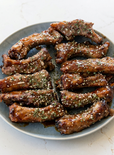 A plate full of ribs for kids covered in a hoisin-based sauce and sprinkled with sesame seeds and cilantro.