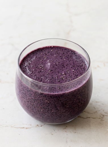 A small glass is filled with a very purple toddler summer smoothie studded with chia seeds.