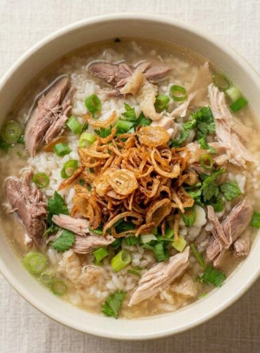A bowl of chicken and rice soup for kids shows pulled chicken pieces emerged in a broth chock full of rice, scallions, and fried onion strings.