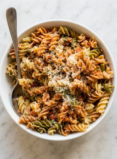 A bowl of rotini is topped with a red pesto for kids (pesto alla trapanese) and grated parmesan.