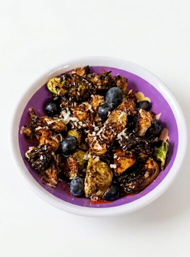 A small bowl of brussels sprouts for kids with crisp ridges is shown; blueberries and grated parmesan are also visible atop the sprouts.